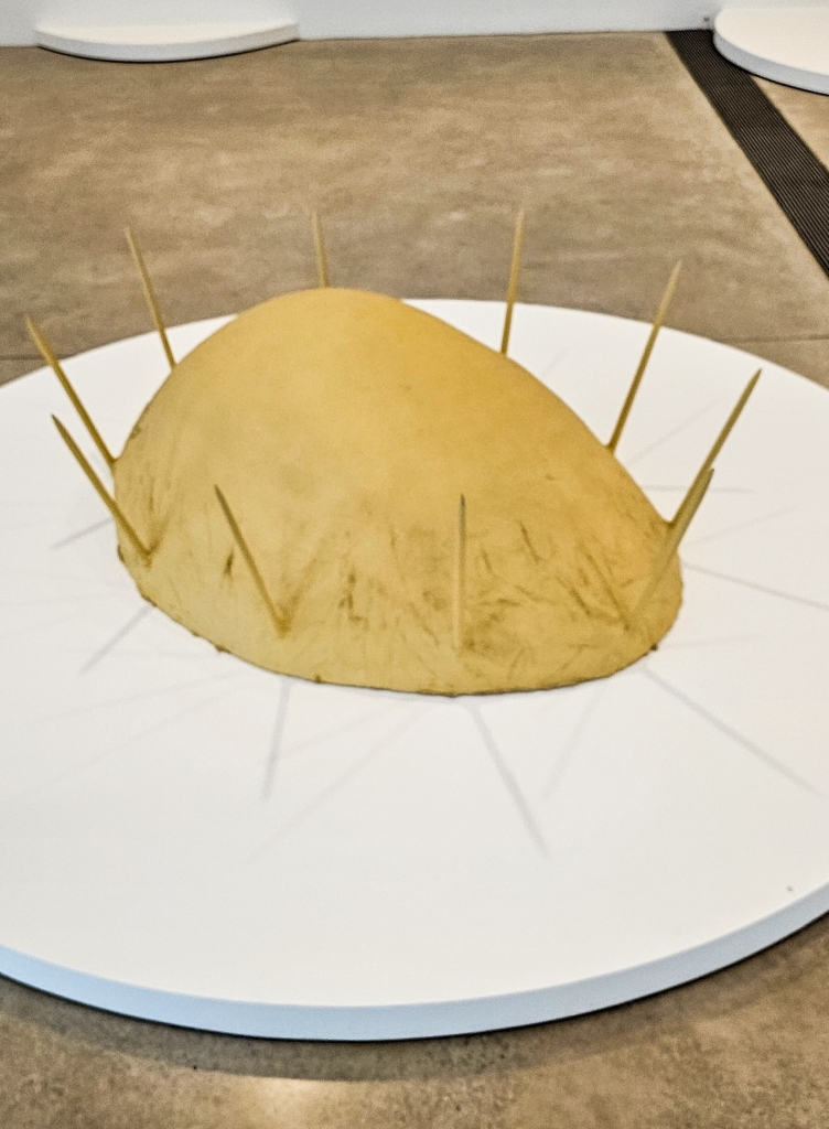 Rounded sculpture, flat on the bottom, in beige, with pointed spines jutting out of its perimeter
