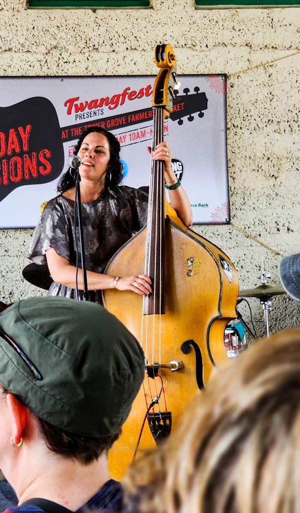 Light skinned woman playing upright bass, crowd in foreground

