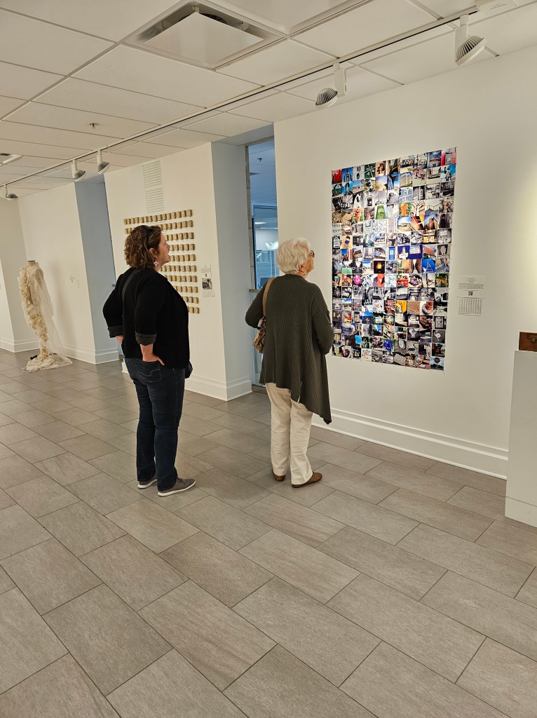 A woman and her daughter looking at an arrangement of photographs on a gallery wall.